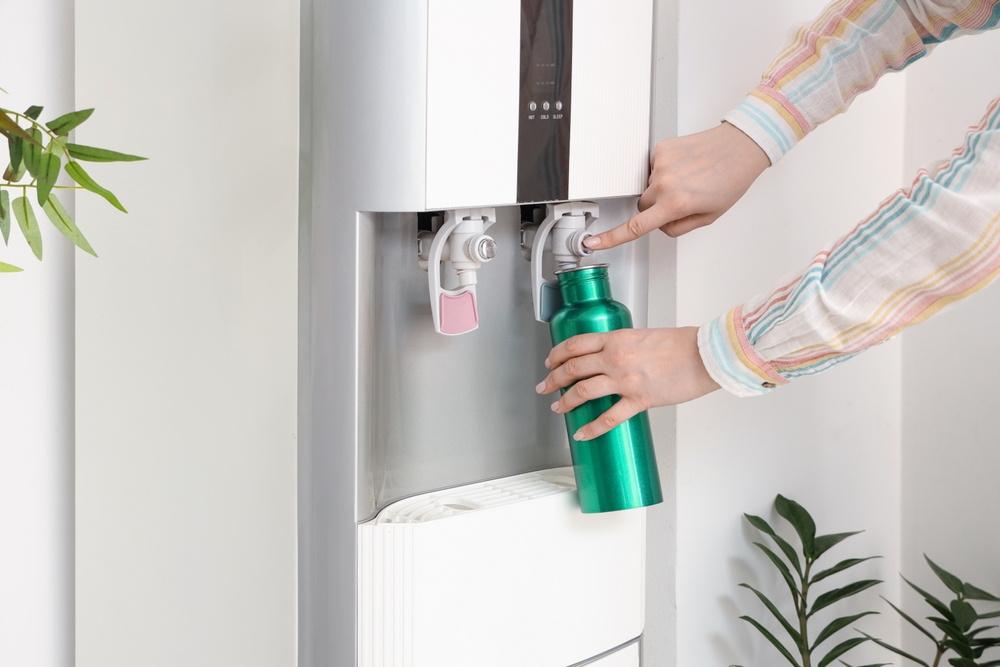 Woman,filling,green,bottle,with,filtered,water,from,cooler,near